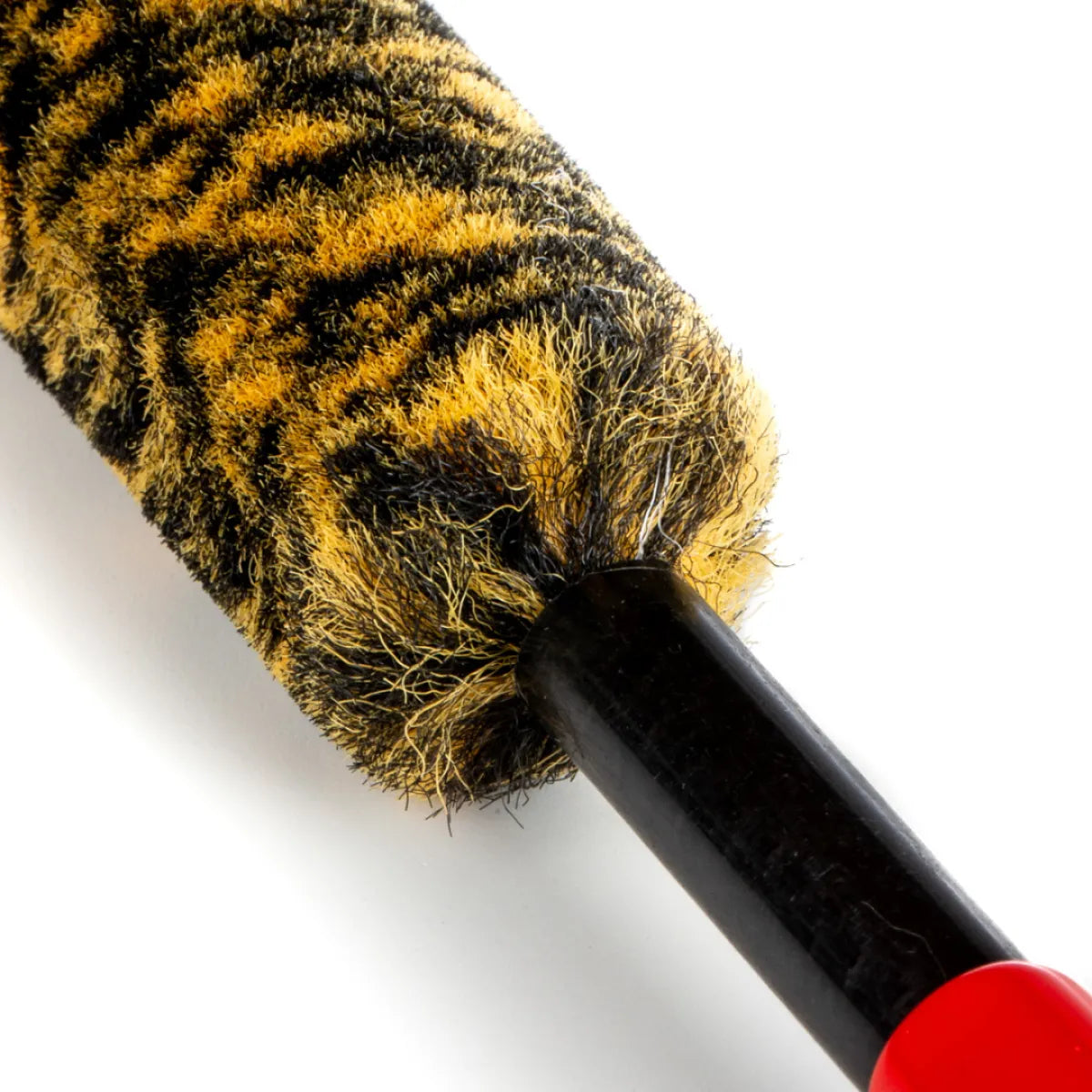 Close-up van een verfroller met tijgerstreeppatroon, lijkend op een velgenborstel, en een zwart handvat met rood uiteinde op een witte achtergrond.