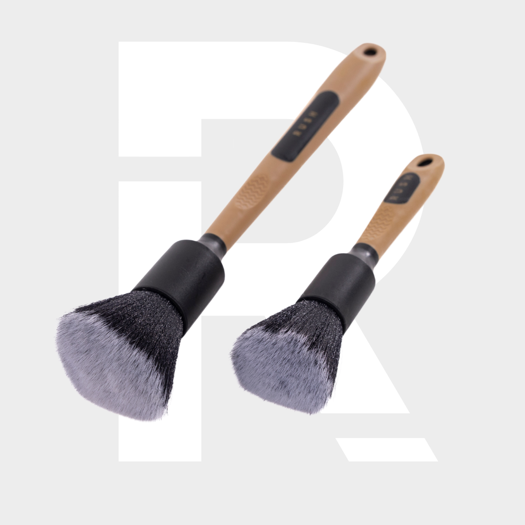 Two Soft Interior Brush Set makeup brushes with light brown handles and superzachte haren are placed diagonally on a light gray background featuring a large, faint white letter R.