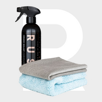 A black spray bottle labeled Ceramic Sealant Package stands behind two folded microfiber towels—one gray and one light blue—on a plain light background.