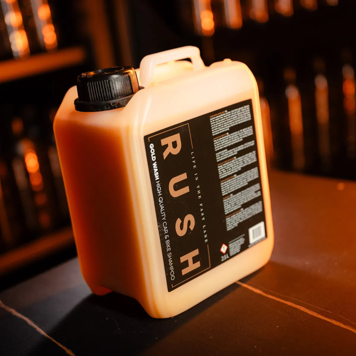 A large plastic container labeled Gold Wash 2,5 liter sits on a surface in warm lighting, featuring a black screw cap and top handle. The label provides product details and instructions.