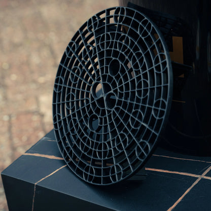 A black plastic grit guard from the Bonus Bucket Kit leans against a dark bucket on tiles, with a blurred background.