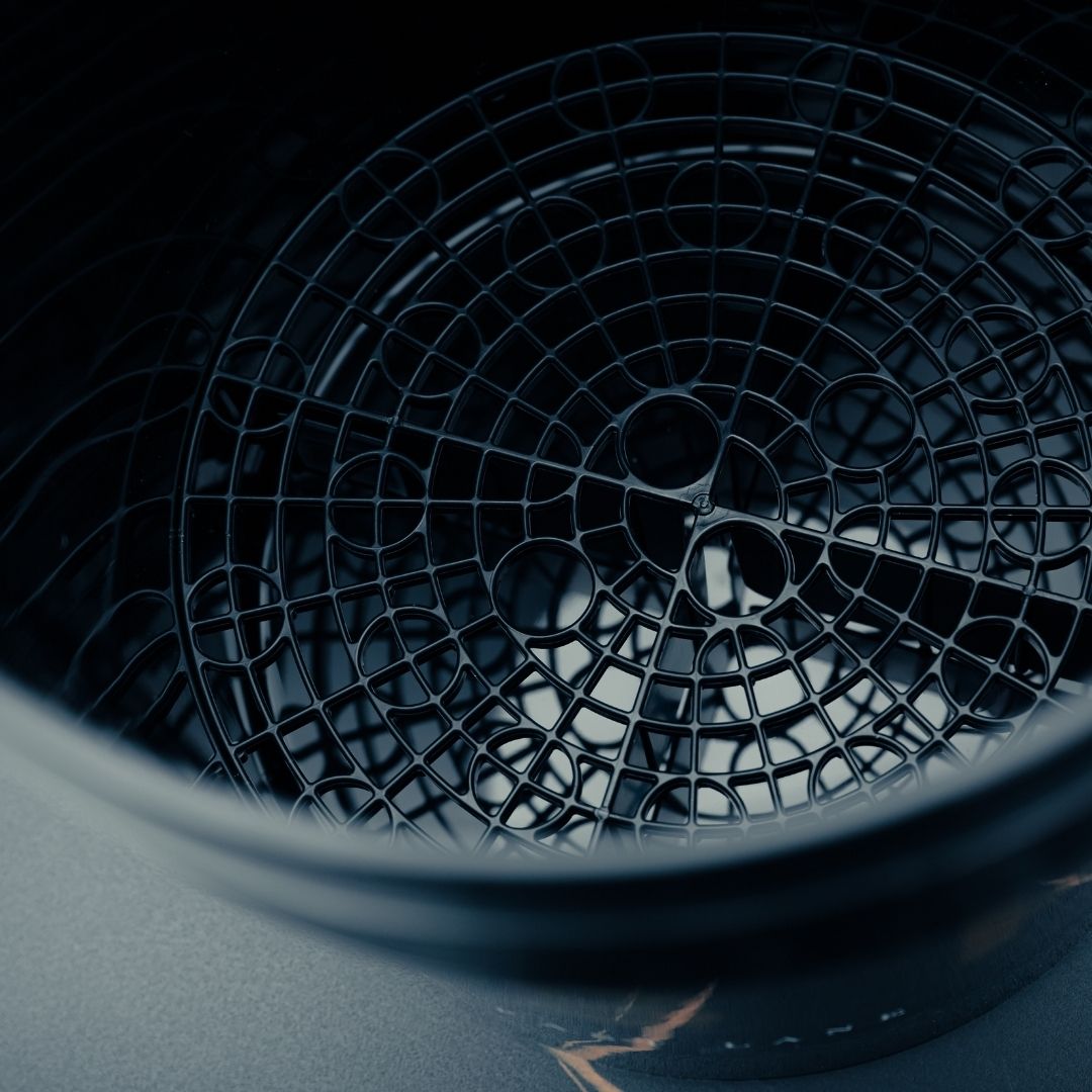 Close-up of a Grit Guard, a round black plastic insert with circular and radial patterns, placed inside a large dark container.