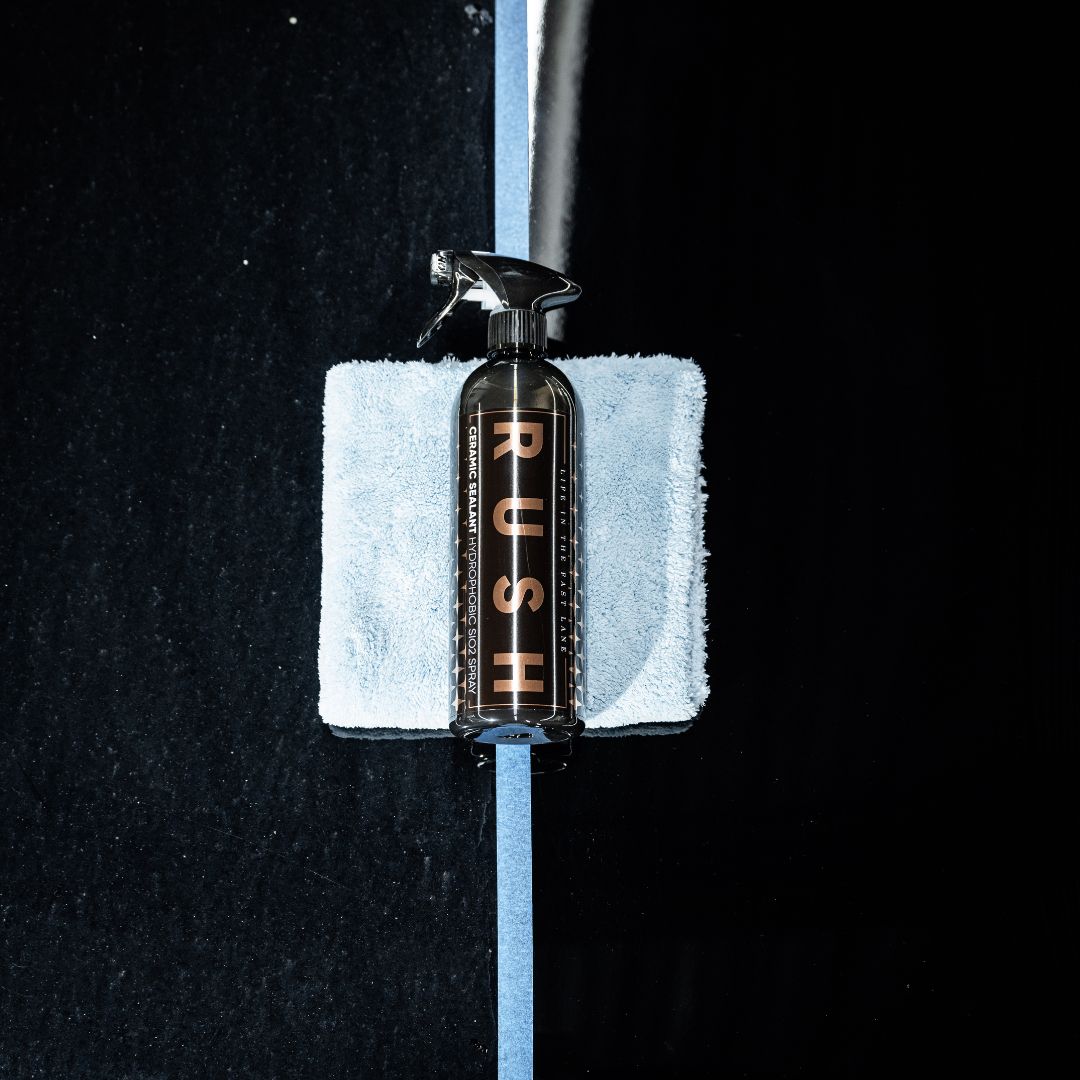 A spray bottle labeled Winter Protect DEAL, designed for winter protection, rests on a folded light blue microfiber cloth atop a reflective black surface divided by a strip of blue tape.
