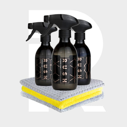 The Interior Sample Package includes three black RUSH spray bottles arranged behind two neatly folded microfiber cleaning cloths, one gray and one yellow, set against a light gray background with a large white "R".