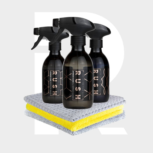 The Interior Sample Package includes three black RUSH spray bottles arranged behind two neatly folded microfiber cleaning cloths, one gray and one yellow, set against a light gray background with a large white "R".