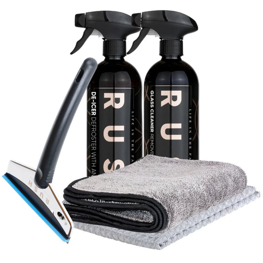 The Window Clear Winter Kit includes two black RUSH spray bottles, an IJskrabber squeegee with a blue edge, and two folded microfiber towels—one dark gray and one light gray—arranged on a white background.
