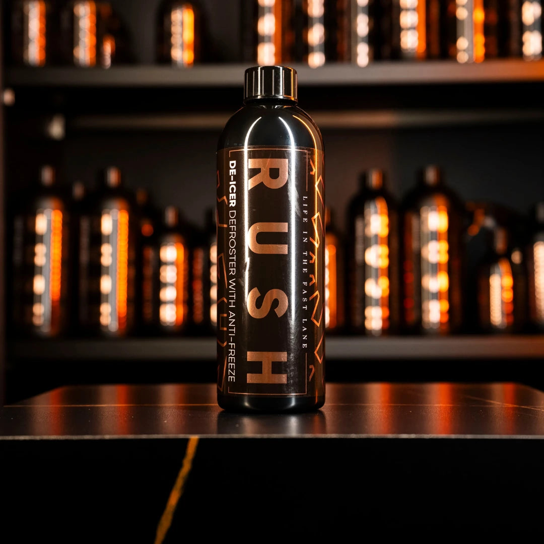 A black bottle labeled Window Clear Winter Kit rests on a black surface, with other similar bottles blurred in the background and all illuminated by warm orange lighting.