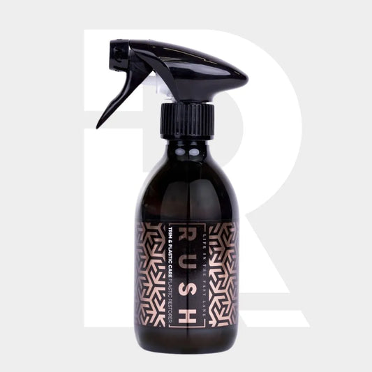 A black spray bottle labeled Trim & Plastic Care with a geometric pattern, perfect for bumper and kunststof exterieuronderdelen onderhoud, stands against a light gray background featuring a large, faint white R.